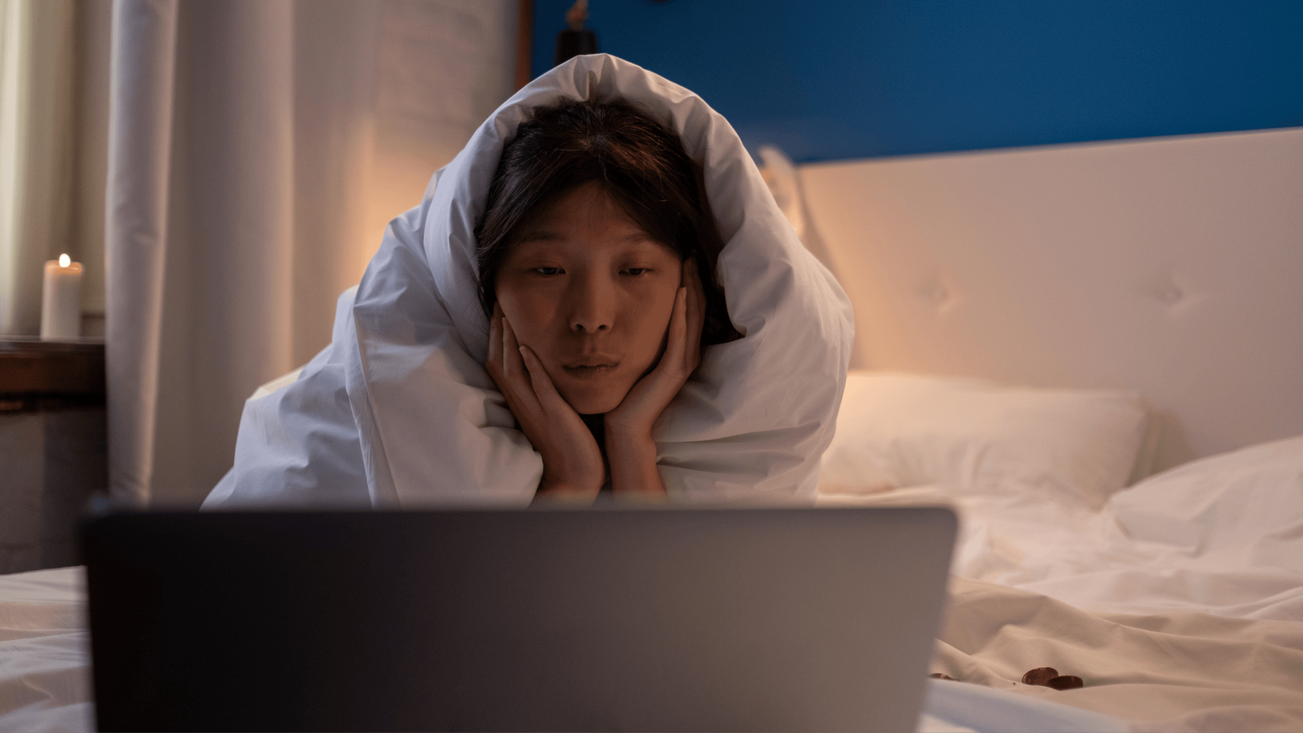A woman wrapped in a blanket, sitting alone at night, illuminated by a laptop screen — symbolizing emotional survival and protecting warmth in a cold world.