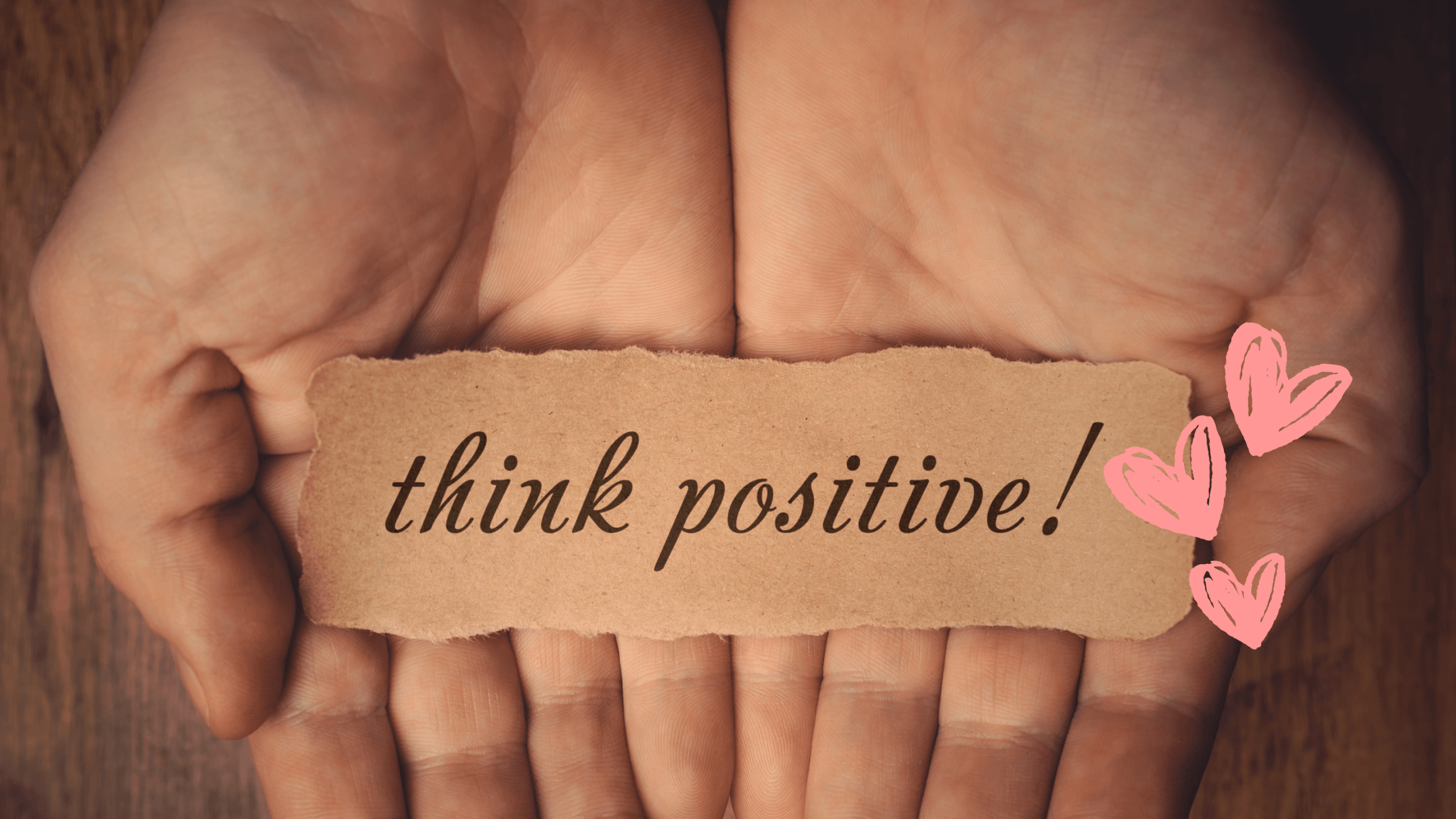 Two hands holding a note that says “Think Positive” with pink heart doodles