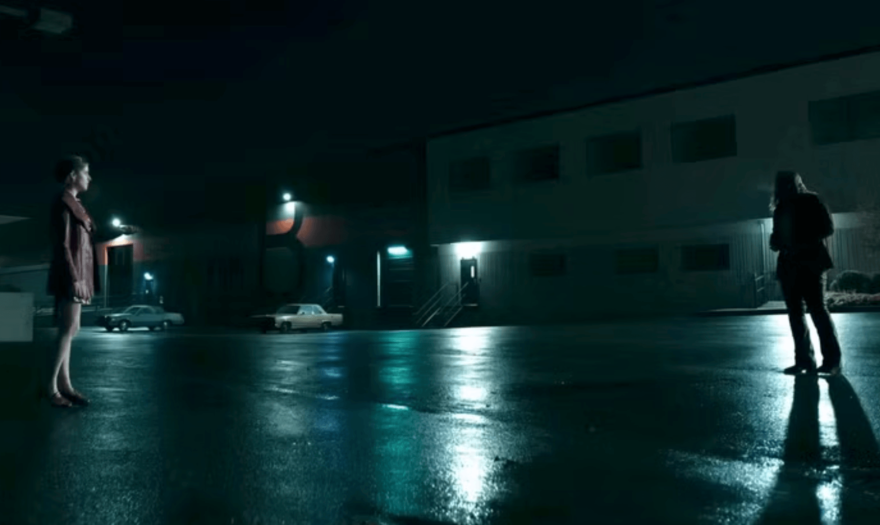 A woman stands alone at night facing a man in a deserted parking lot, a moment of silent tension in Woman of the Hour.