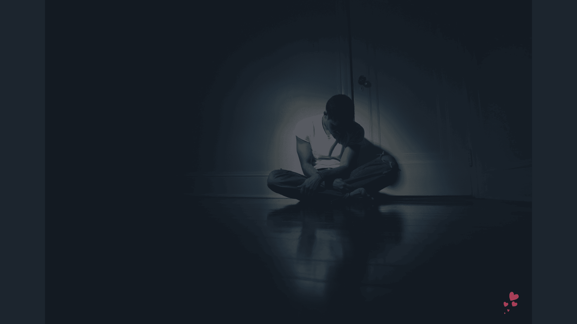 The Male Loneliness Epidemic - A man sits alone on the floor in a dimly lit room, hunched forward in silence and emotional exhaustion.