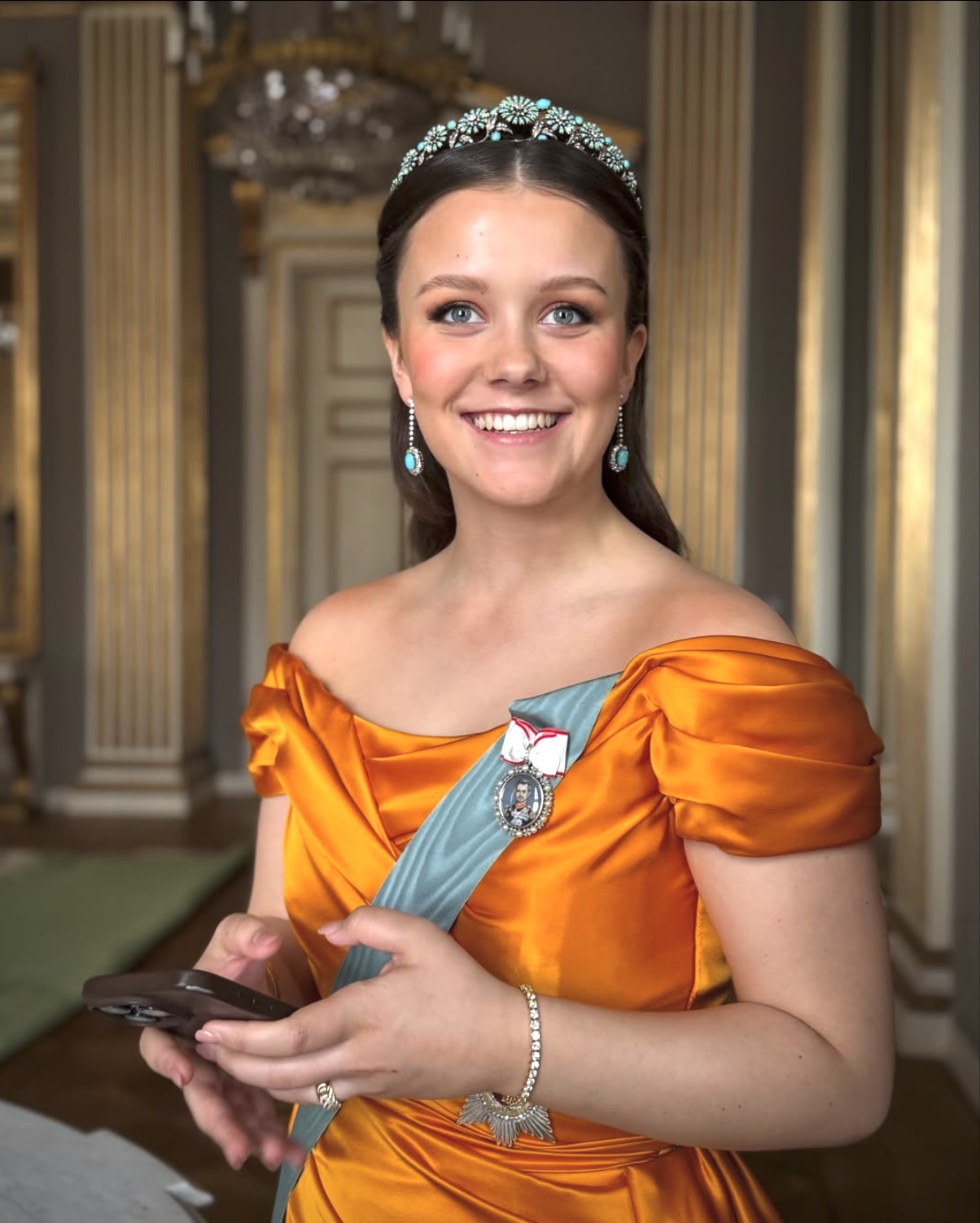 Princess Isabella of Denmark wearing a tiara and sash while holding a smartphone in her official portrait — a Gen Z royal moment that redefines what counts as cultured.