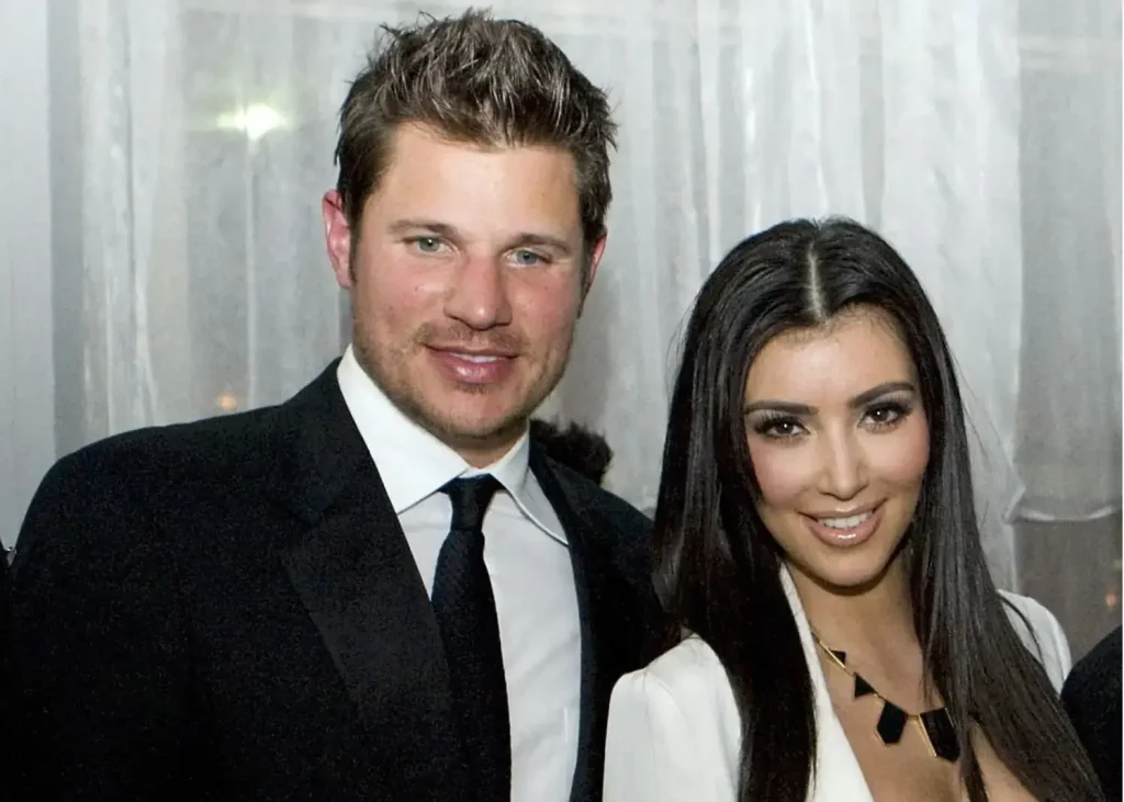 Nick Lachey and Kim Kardashian pose together at a formal event, dressed in a black suit and a white blazer, smiling at the camera.