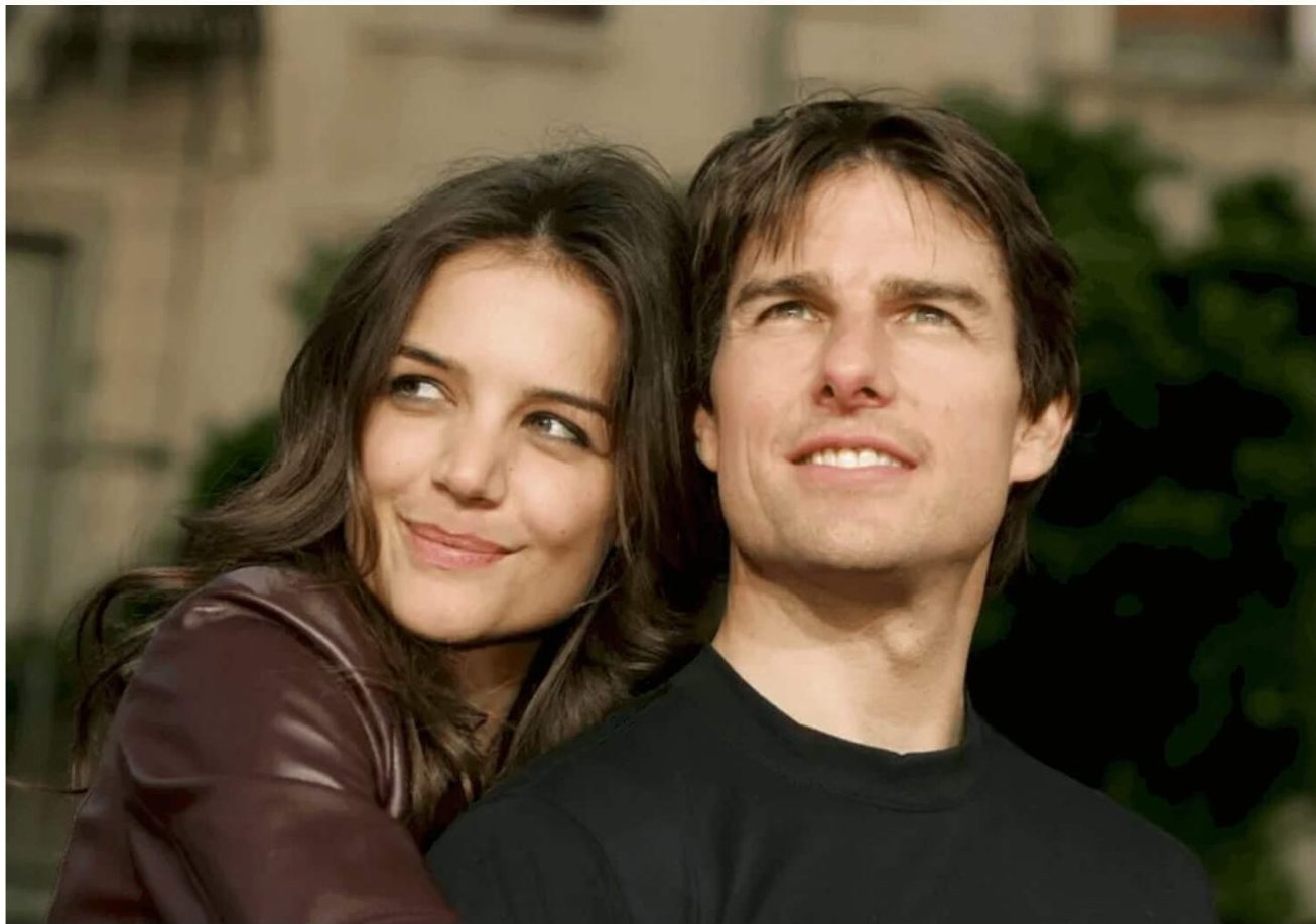 Hollywood Relationship Terms - Katie Holmes and Tom Cruise embrace outdoors, both gazing into the distance with soft smiles, in a moment captured during their highly publicized relationship.