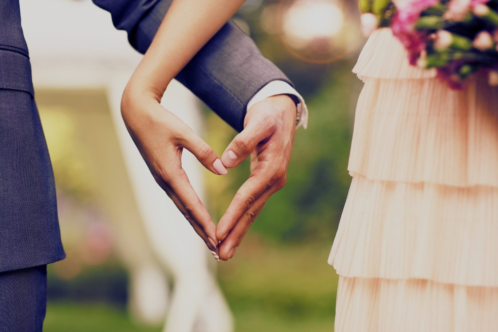 should you invite your ex to your wedding - Close-up of couple forming a heart with their hands, symbolizing new beginnings and emotional commitment