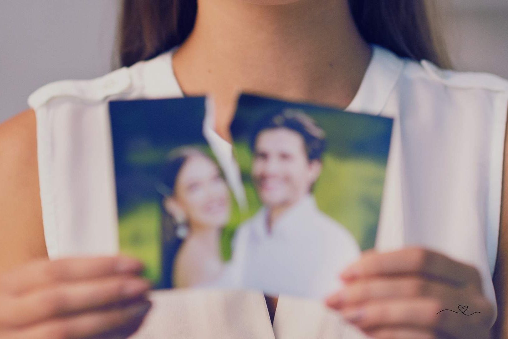 should you invite your ex to your wedding - Woman holding a torn photo of a smiling couple, representing emotional grief after a breakup
