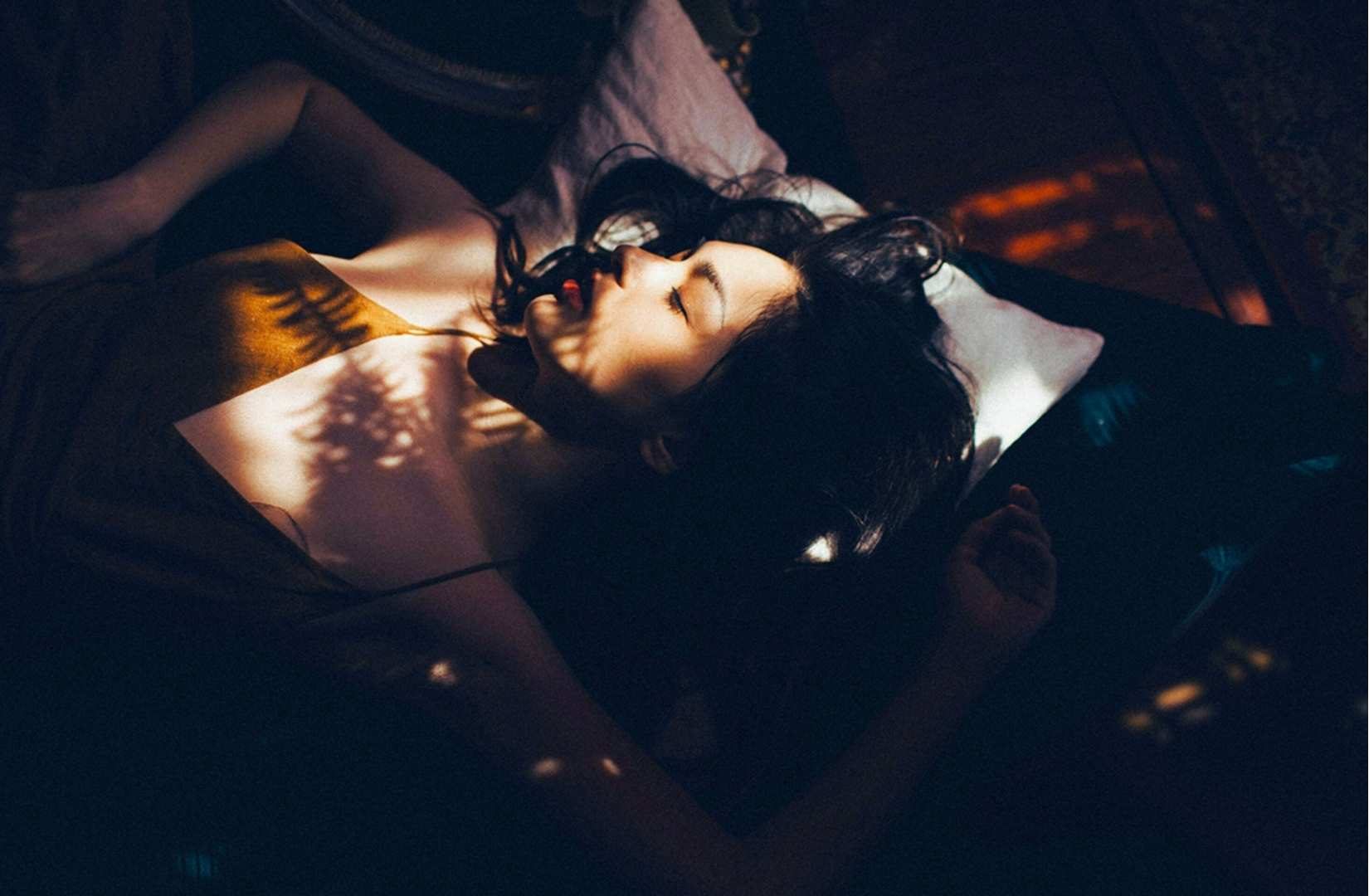 Why Nightmares Happen - A woman lying in bed with eyes closed, touched by soft sunlight and shadows