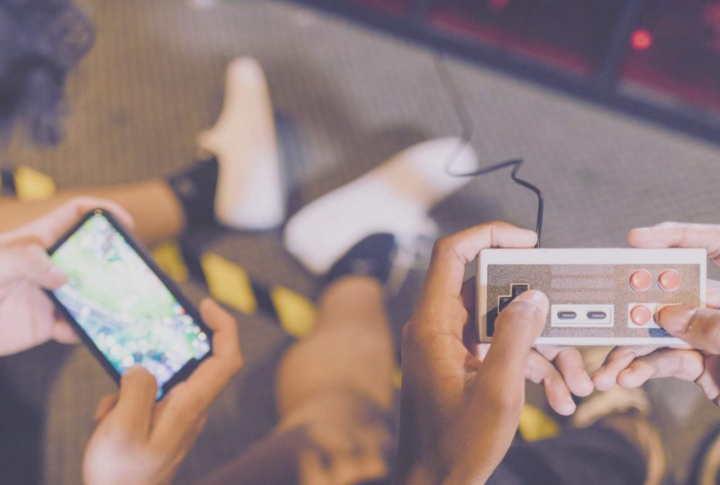 Escapism as survival - Two people immersed in mobile and retro gaming, sitting on the floor, escaping reality through screens.