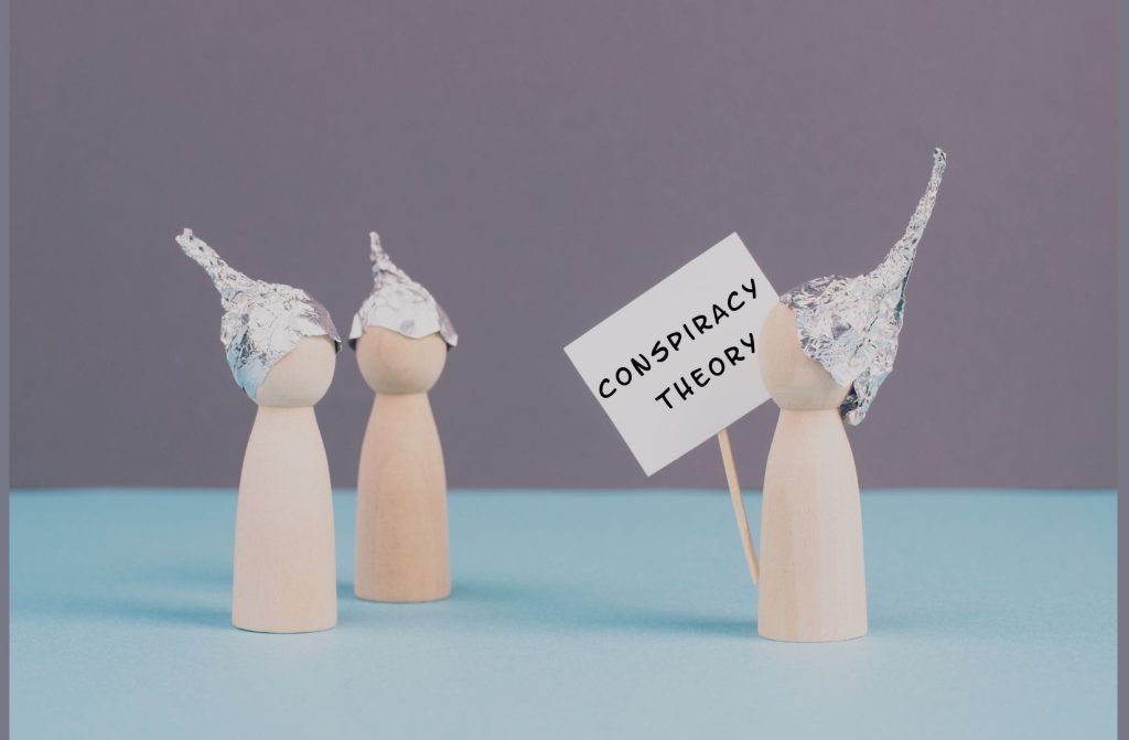 Toddler fear of Alexa - Wooden figurines wearing tin foil hats holding a sign that says conspiracy theory