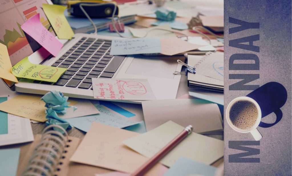 High functioning hot mess – cluttered desk with sticky notes, laptop, and coffee on Monday morning.