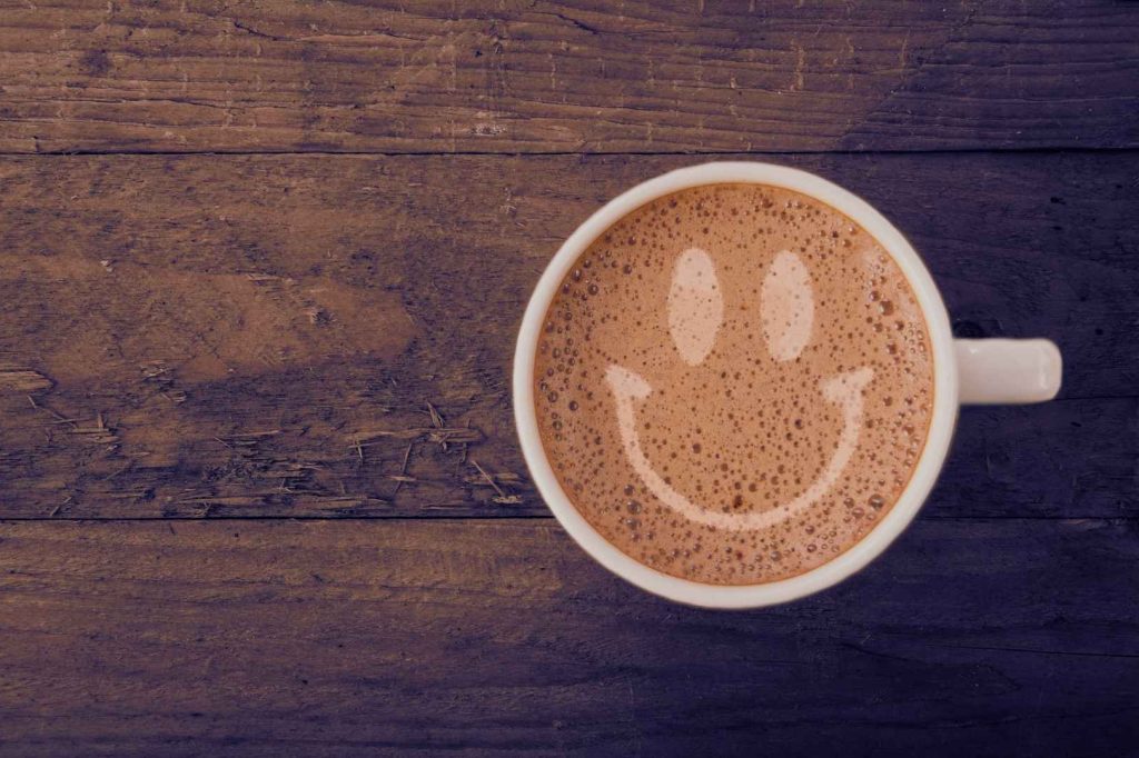 Micro - joys, A cup of coffee with a smiley face foam design on a rustic wooden table, symbolizing small daily joys.