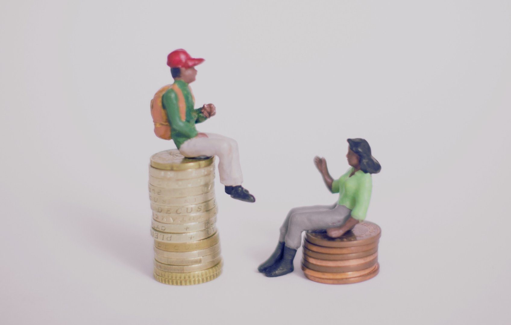 Top-Tier Man - Miniature man and woman on different-sized stacks of coins having a conversation