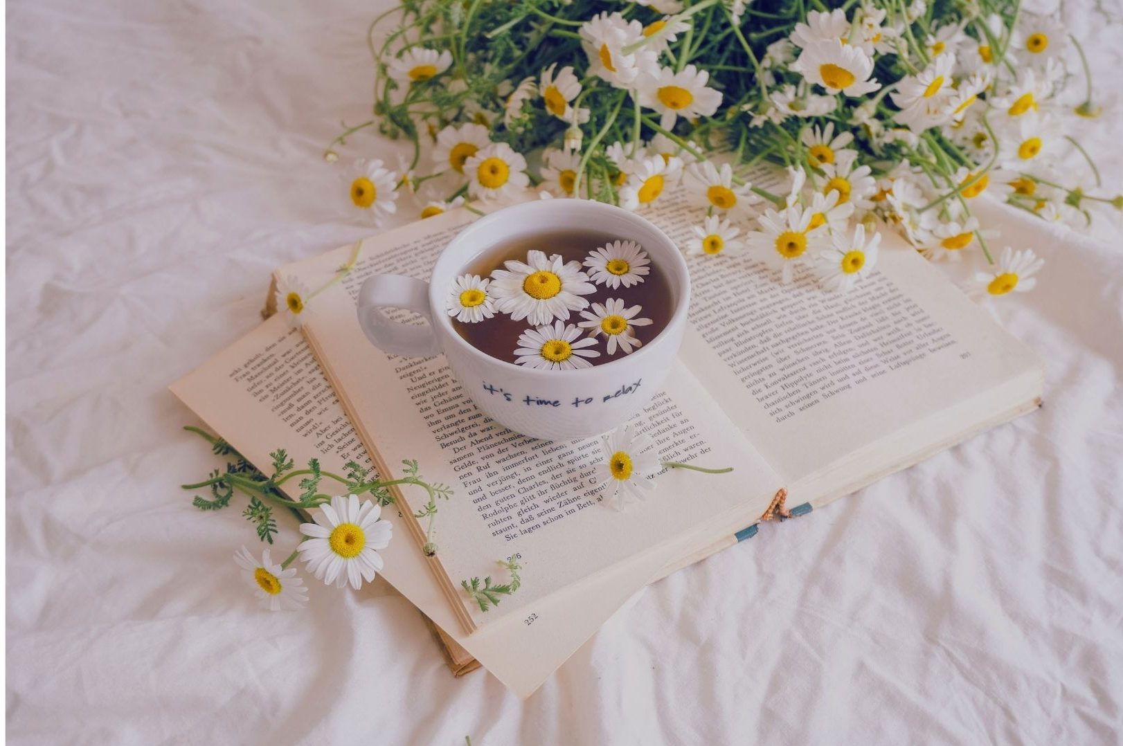 Simple life and social comparison - pastel cup of tea with flowers on an open book in a neatly styled bed.